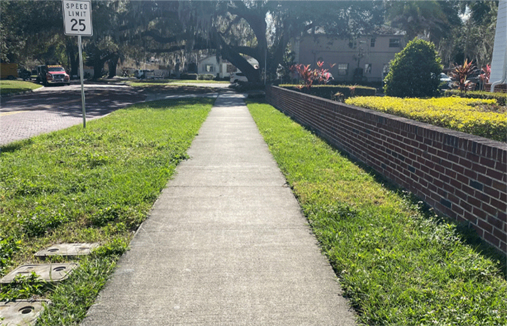 An image of a concrete sidewalk path parallel to a brick wall.