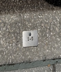 A small square metal on-street parking tag attached to the curb displaying the number “1–5.”