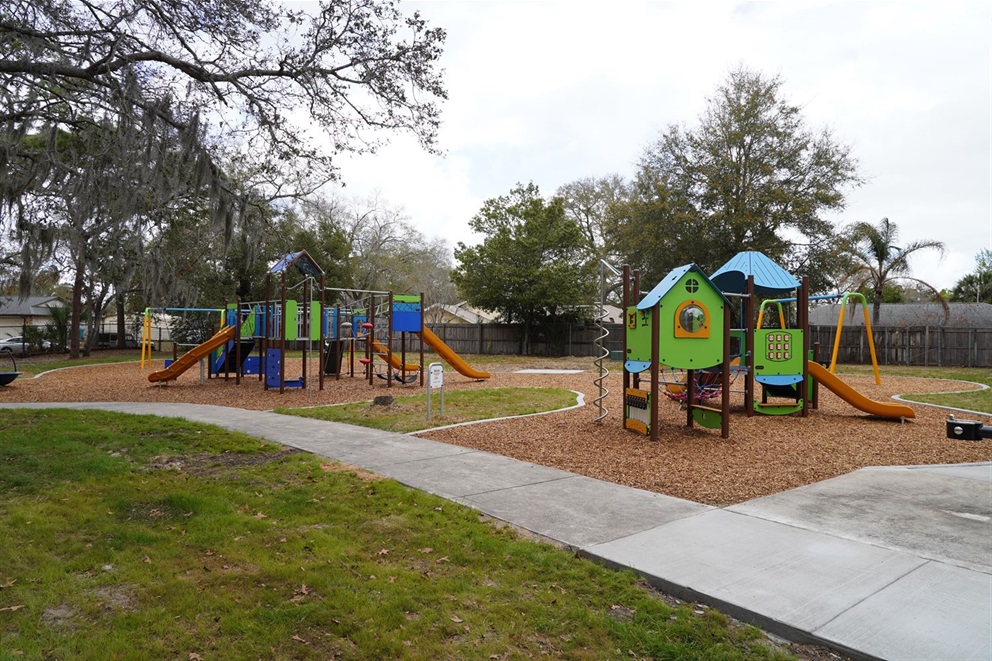 The Playground at signal hill park with two play scapes with slides surrounded by trees with grass mulch and sidewalk.  