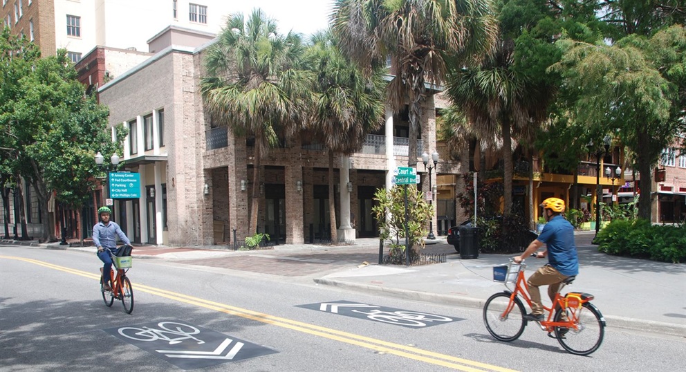 Two cyclists wearing helmets utilize shared bike lanes on Central Boulevard in downtown Orlando.